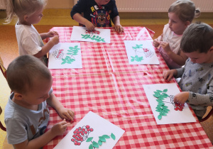 dzieci przy stoliku naklejają czerwoną plastelinę w miejsce grona jarzębiny na kartce
